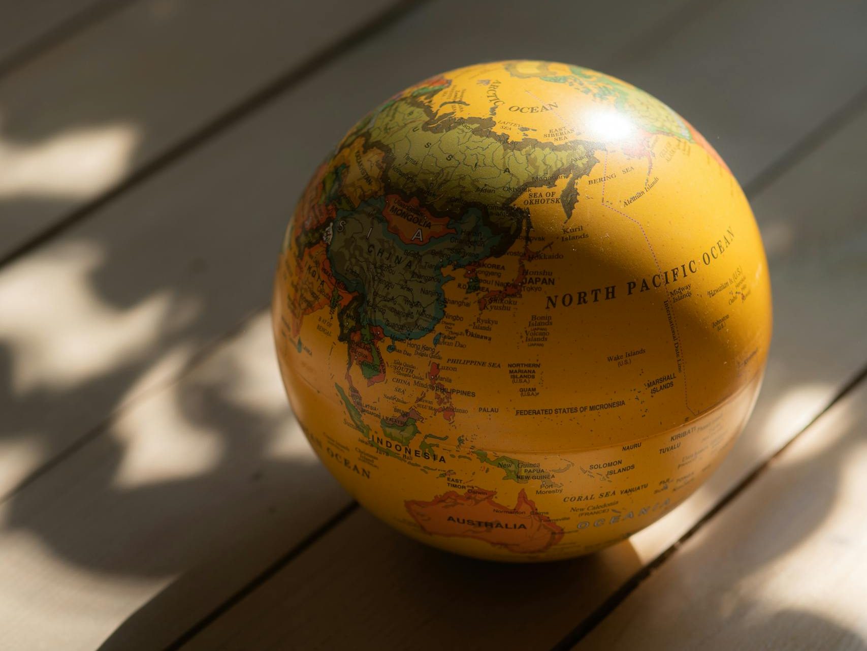A vintage globe with a yellow tint on a wooden surface, casting shadows.